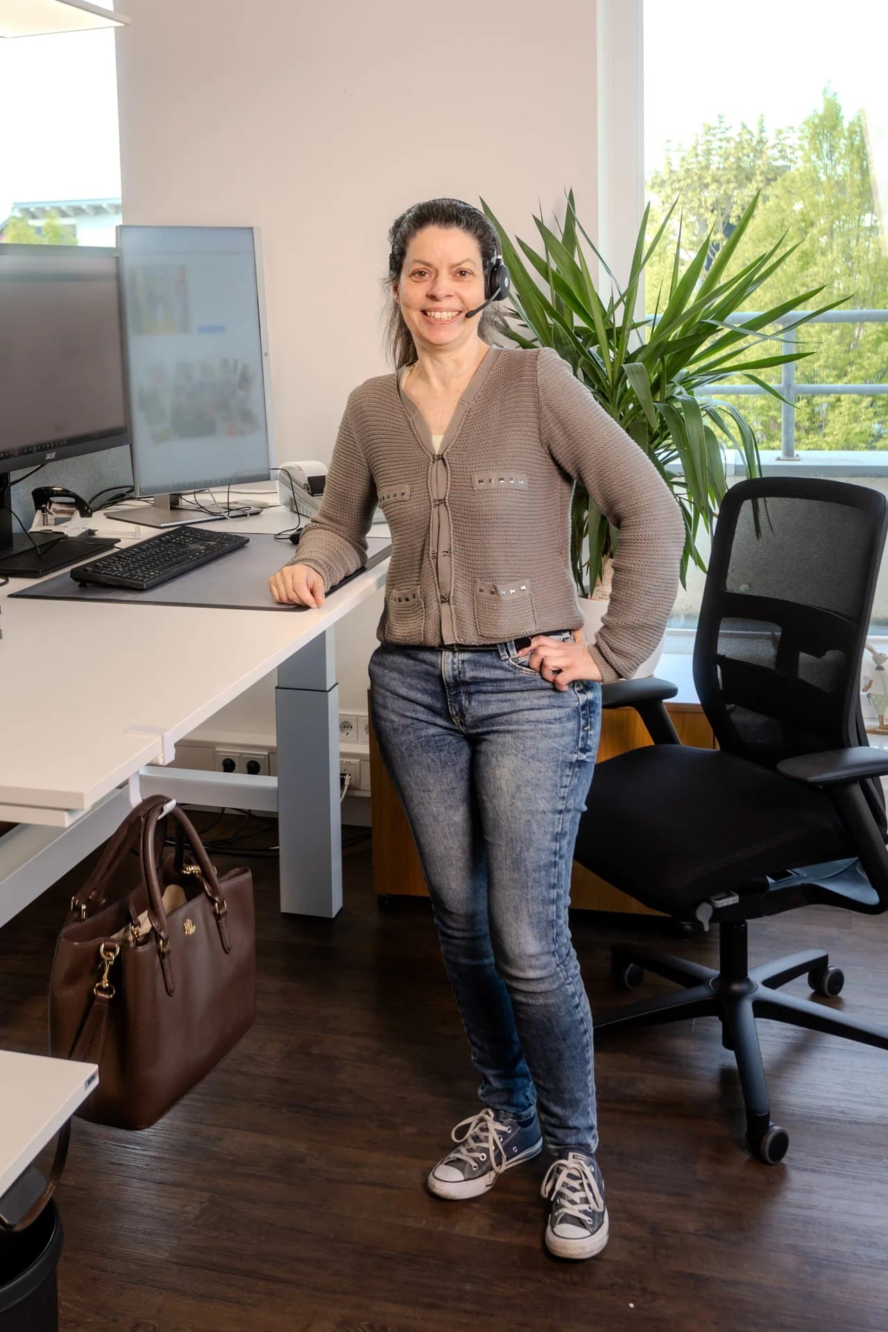 Lächelnde PMPG-Mitarbeiterin mit Headset und Jeans am Schreibtisch