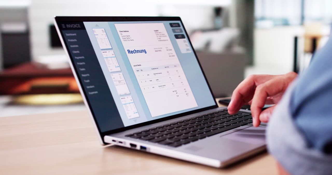 Laptop mit einer Rechnung auf dem Bildschirm, davor eine angeschnittene Person